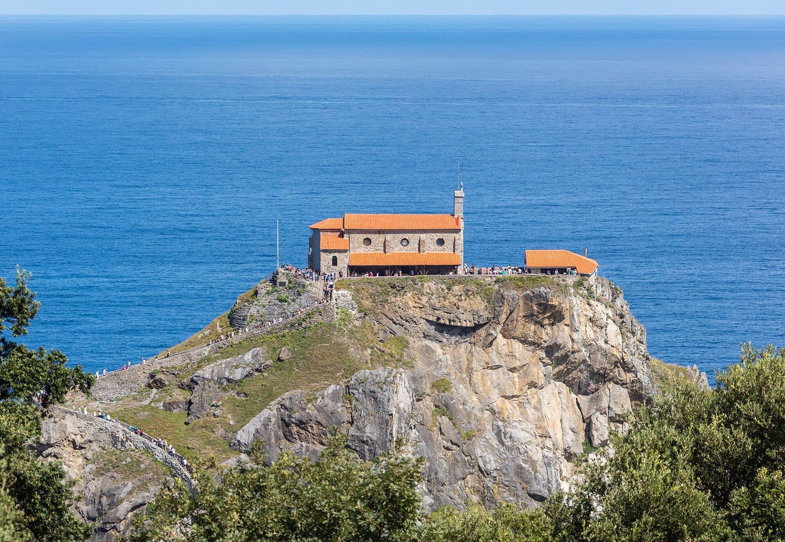 The hermitage of San Juan de Gaztelugatxe on its rocky islet off the Biscay coast, reached by a stone causeway and a stepped path, with the Bay of Biscay behind