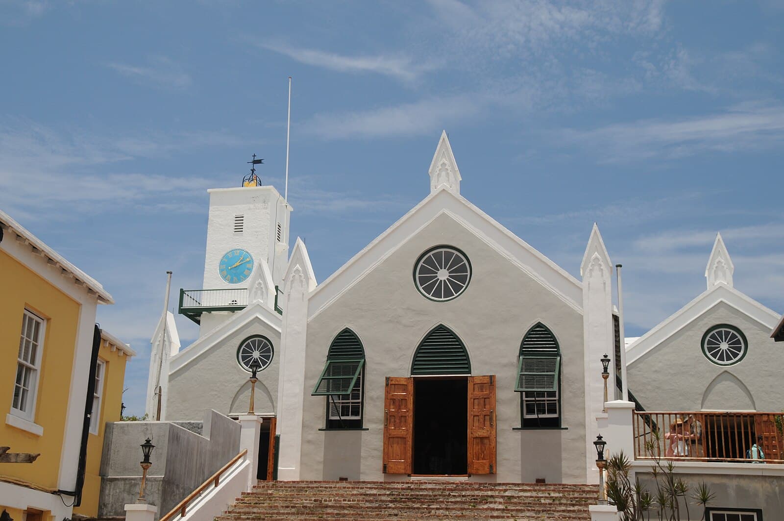 The white limestone front of St Peter's Church in St George's, Bermuda, with its clock tower, arched green-shuttered windows and brick steps rising to the open doors