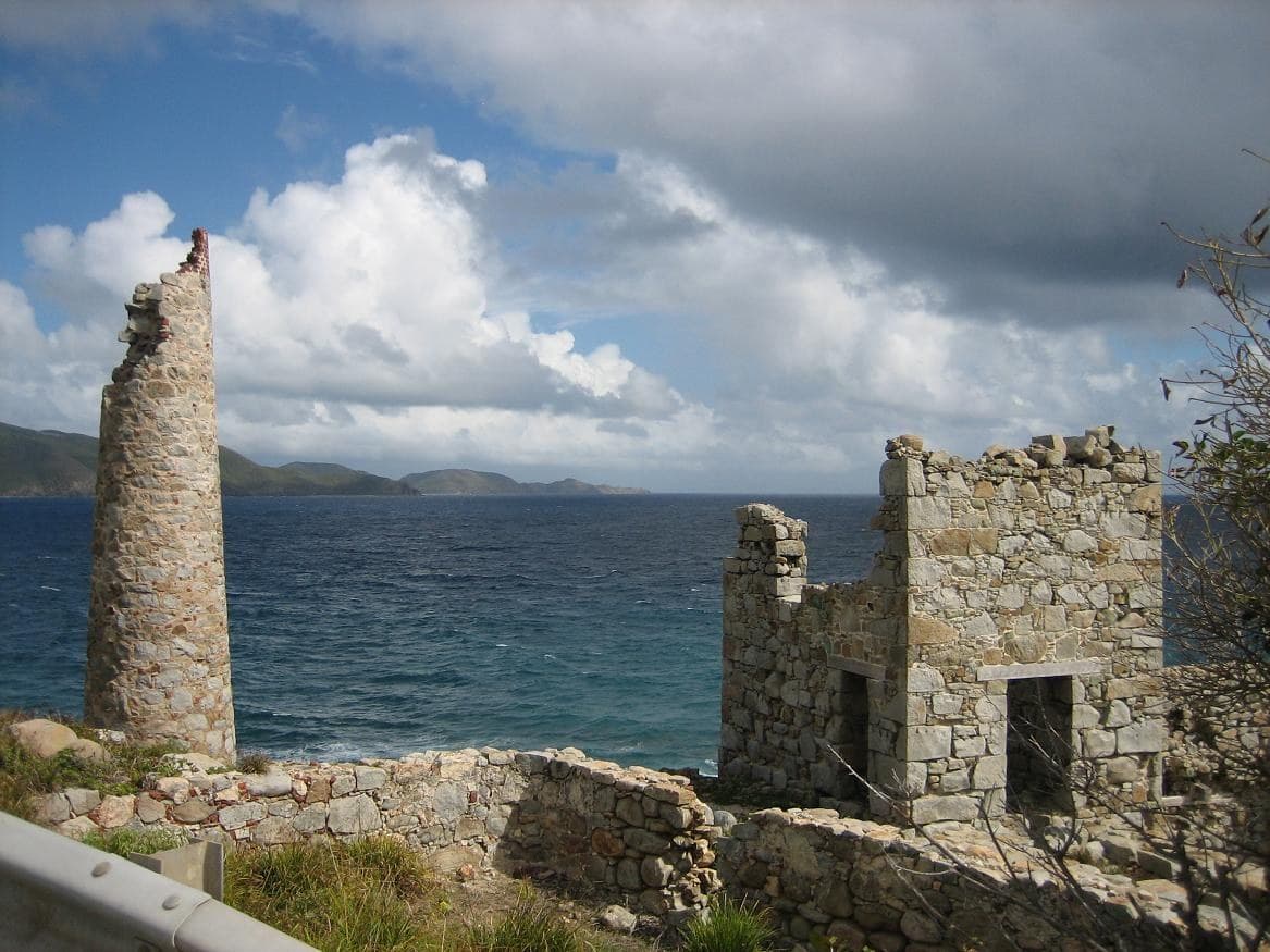 The stone chimney stack and roofless engine house of the nineteenth-century copper mine on the cliffs at Copper Mine Point, Virgin Gorda, with the sea and neighbouring islands behind