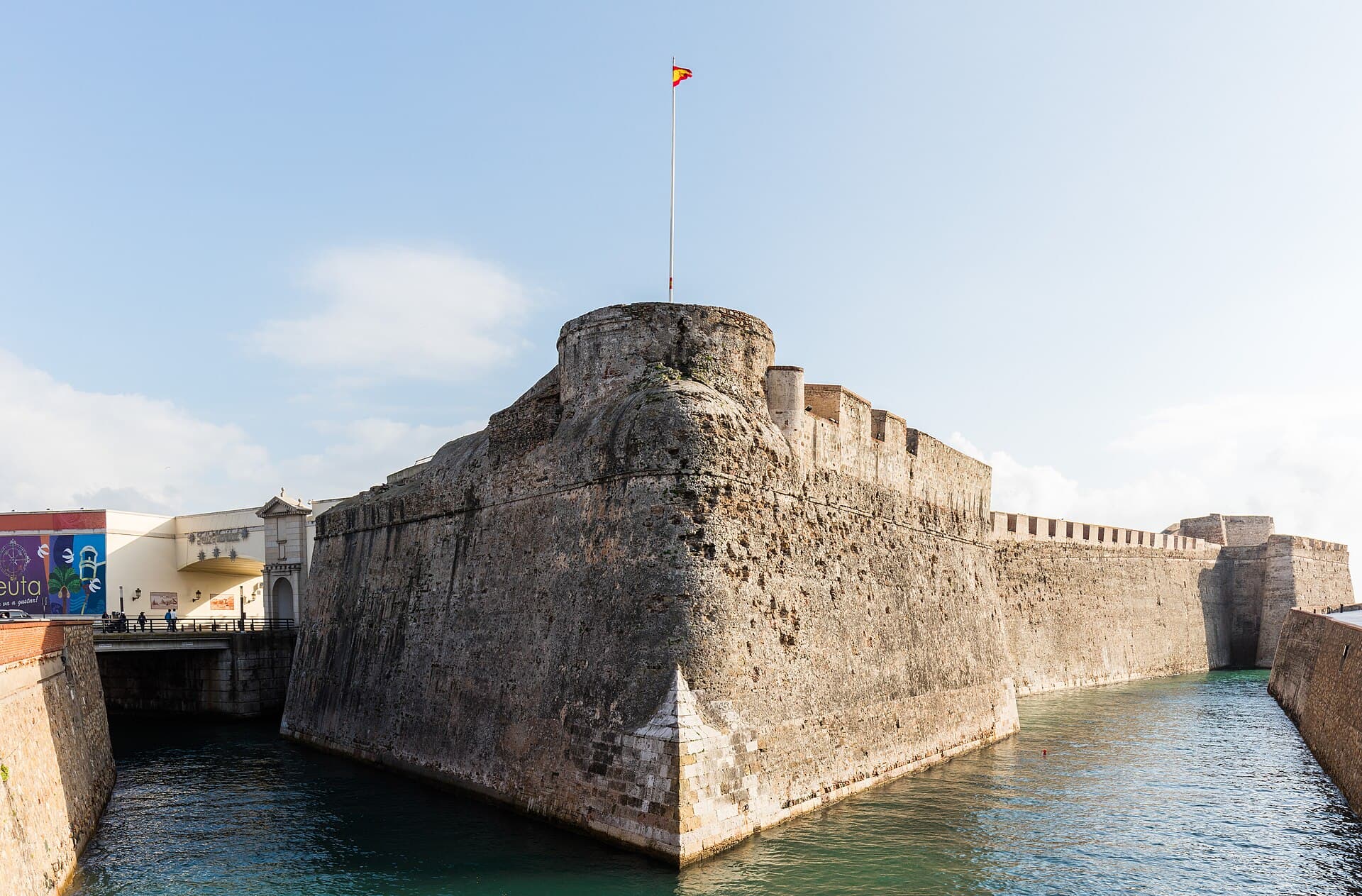 A bastion of the Royal Walls of Ceuta rising from the seawater moat, with the crenellated curtain wall running away to the right