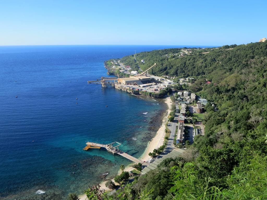Flying Fish Cove seen from the cliffs above, with houses along the shore, the jetty, the phosphate loading cantilever and rainforest running down to the sea