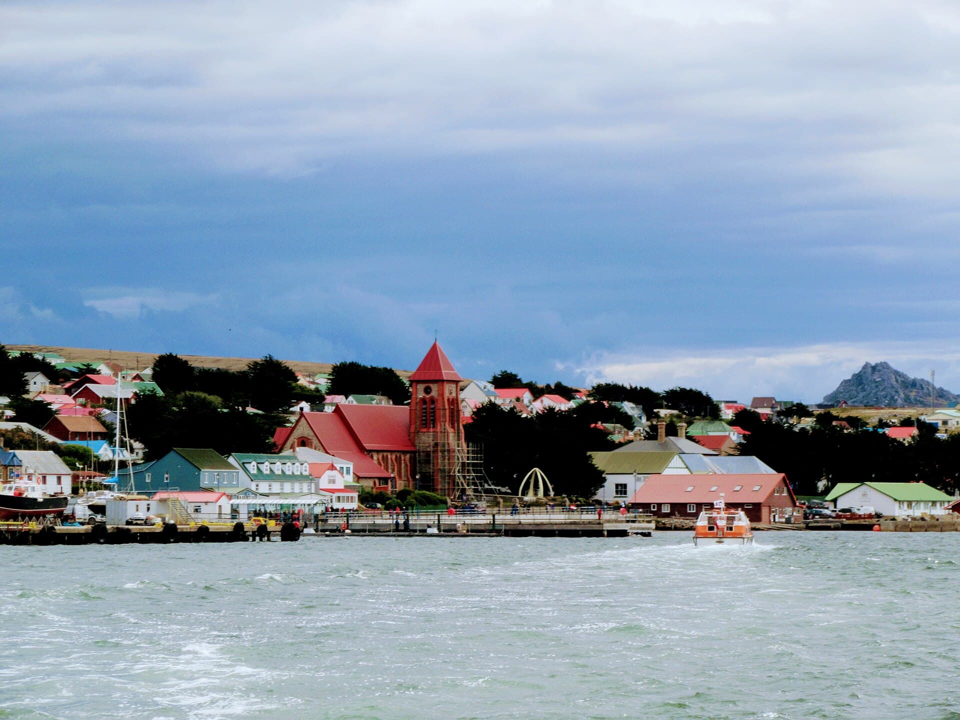 The Stanley waterfront from the harbour, with Christ Church Cathedral's brick tower and red roof, the whalebone arch beside it, and rows of brightly roofed houses
