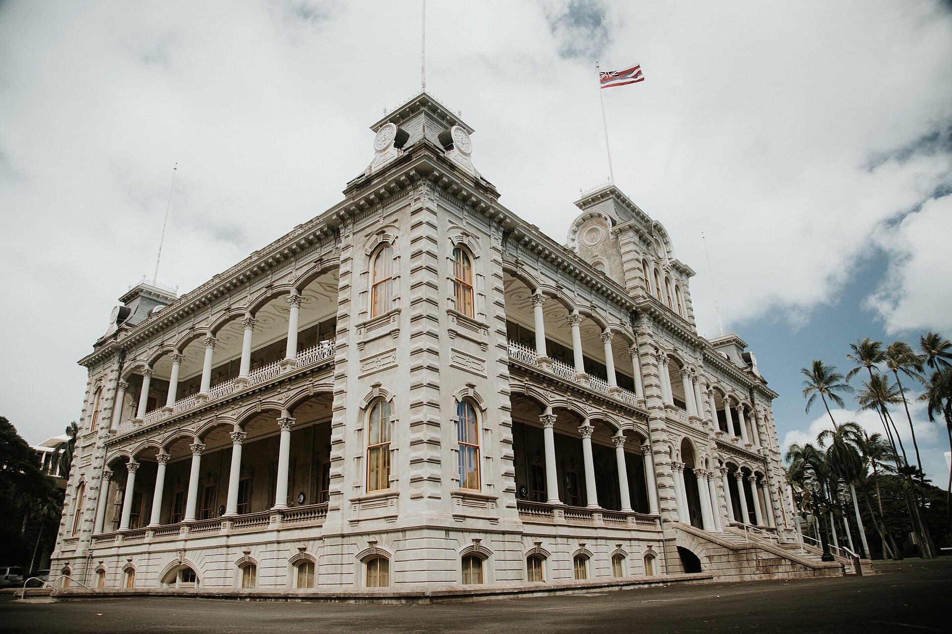 The facade of ʻIolani Palace in Honolulu seen from below, the Hawaiian flag flying beside it