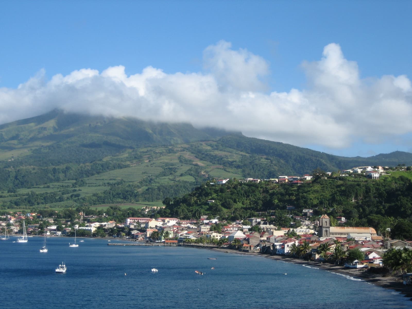 The town of Saint-Pierre on the north-west coast of Martinique, its roofs along a black-sand bay, with the green slopes of Mount Pelée rising into cloud behind it