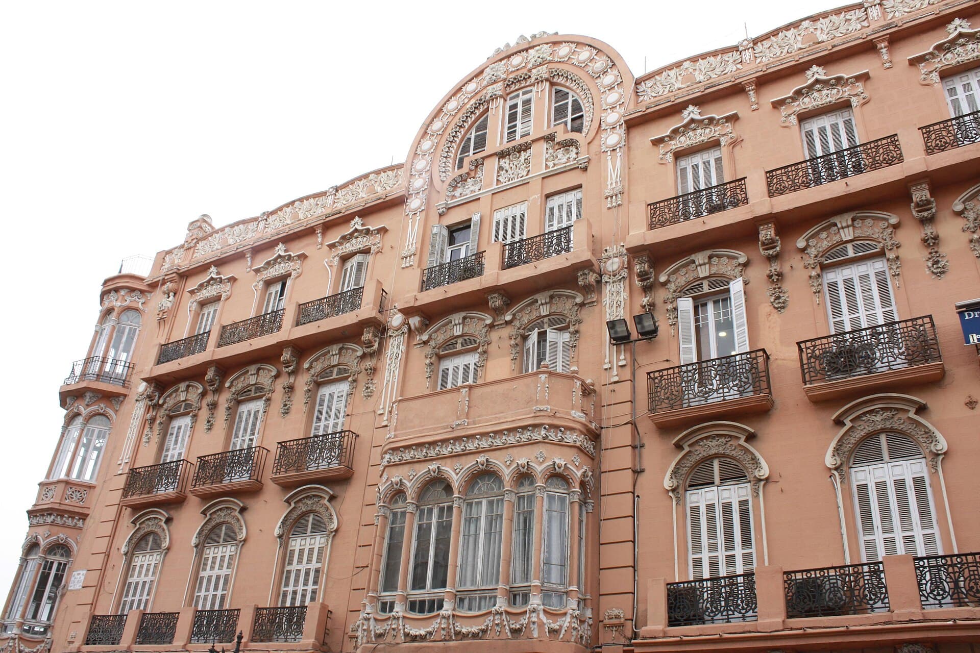 The ornamented pink stucco facade of Casa Melul in Melilla, with floral modernista mouldings, wrought-iron balconies and an arched gable