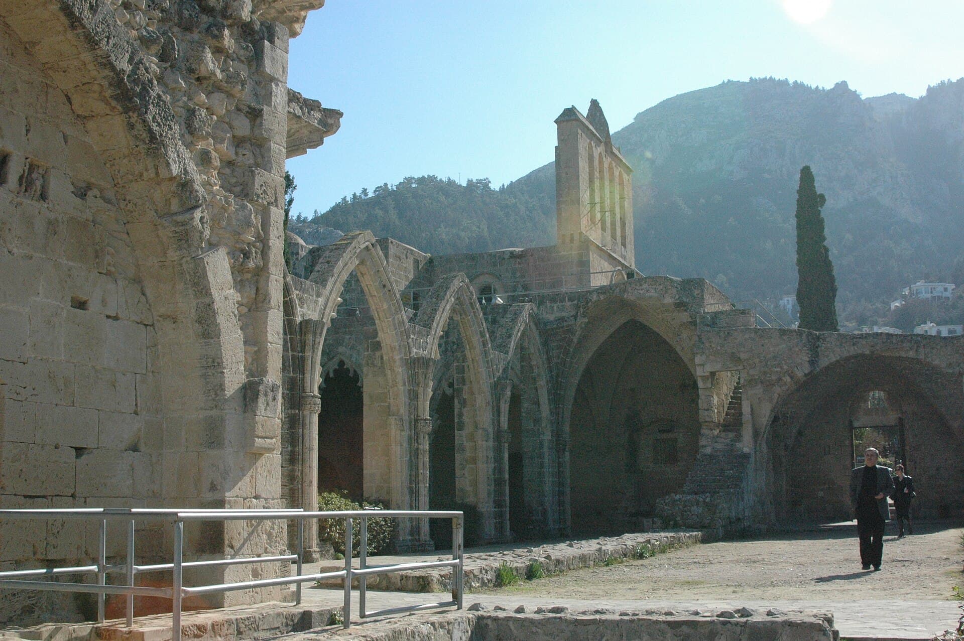 The ruined Gothic arcade and tower of Bellapais Abbey above Kyrenia, with a cypress tree and the wooded slopes of the Kyrenia mountains behind