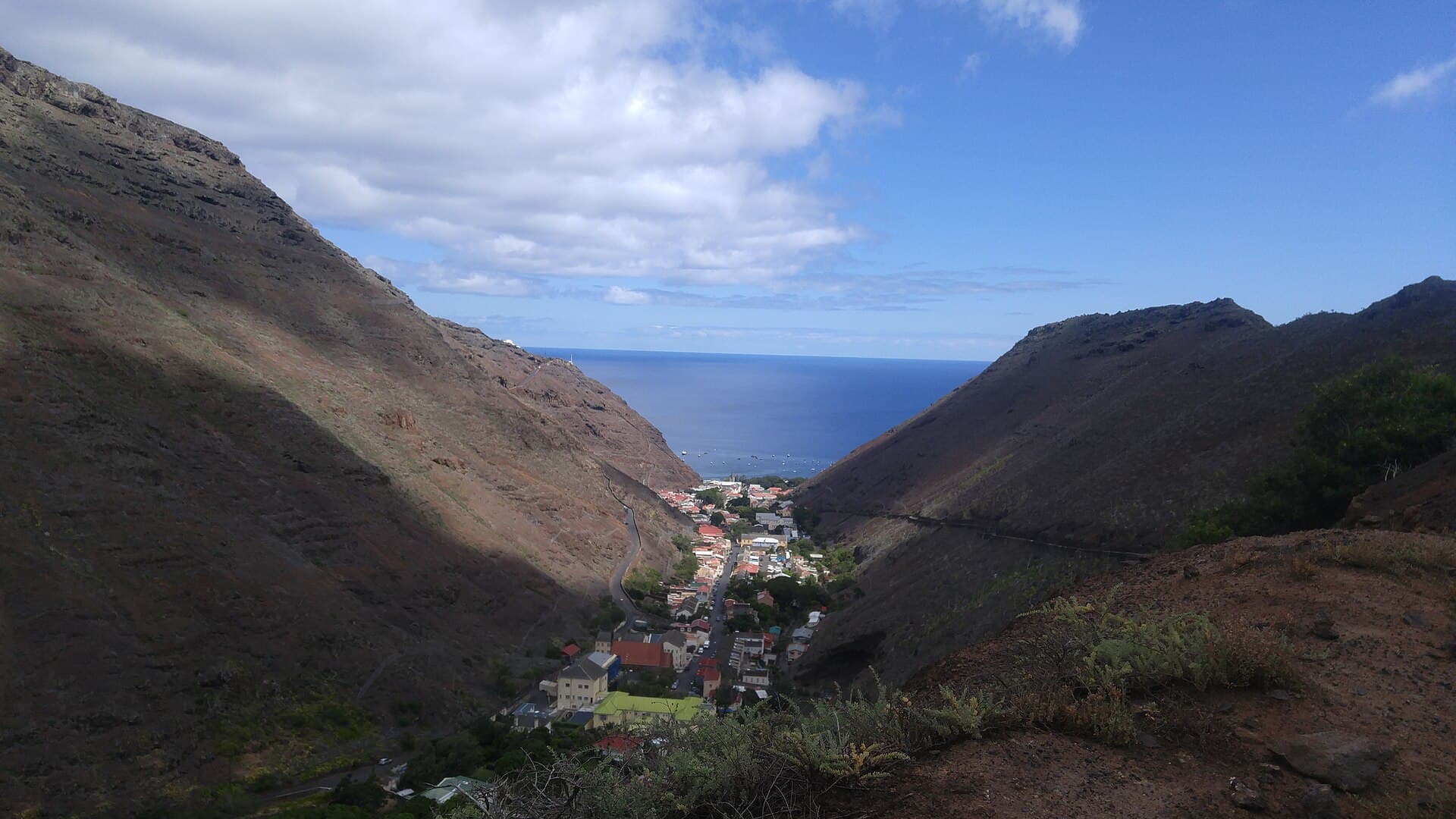 Jamestown, Saint Helena, seen from the hills to the south, its houses packed into a narrow valley between bare volcanic ridges with the anchorage and open ocean beyond