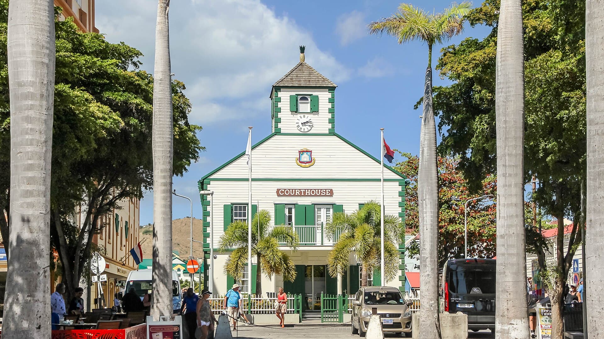 The eighteenth-century courthouse on Wathey Square in Philipsburg, Sint Maarten, a white timber building with green shutters, a clock and bell tower and a carved pineapple finial, seen down a row of royal palms from Front Street