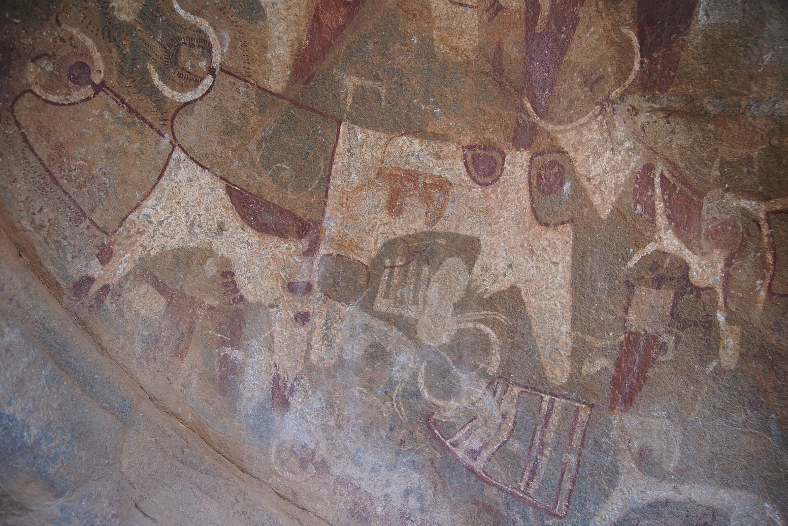 Polychrome rock paintings at Laas Geel showing long-horned cattle with decorated necks alongside smaller human figures, on the curved granite ceiling of a rock shelter