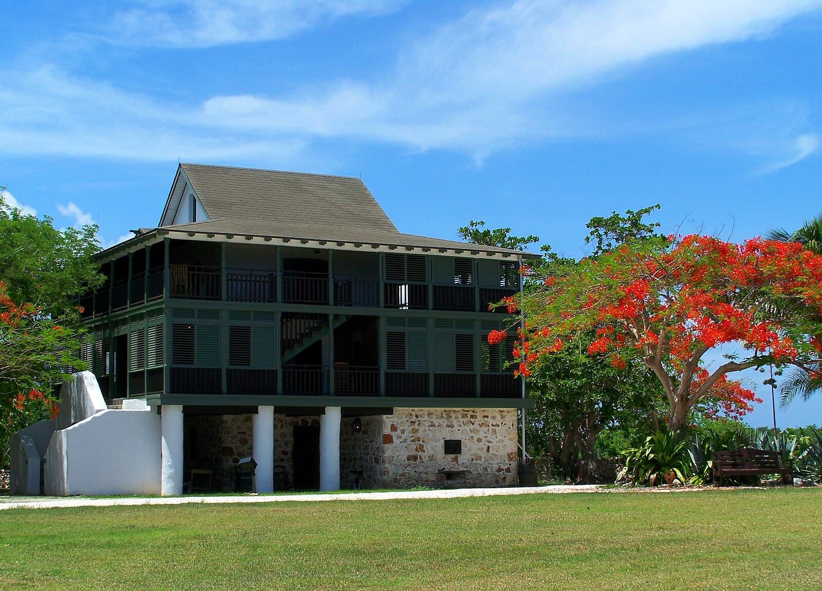 The restored Pedro St James great house at Savannah, Grand Cayman, its dark timber verandahs raised on a coral-stone lower storey, with a royal poinciana in flower beside it