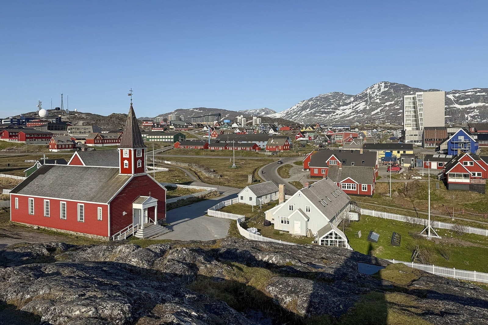 The red timber Church of Our Saviour in Nuuk's old harbour quarter, with the modern town and snow-streaked mountains behind