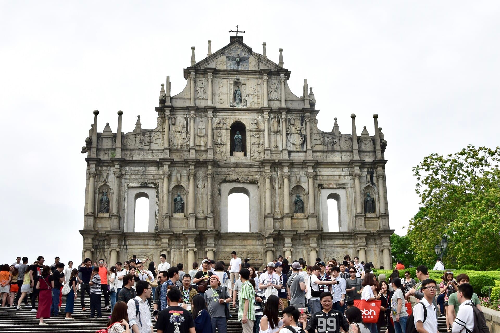 The stone facade of the Ruins of St Paul's in Macau seen from the foot of its granite staircase, with visitors on the steps