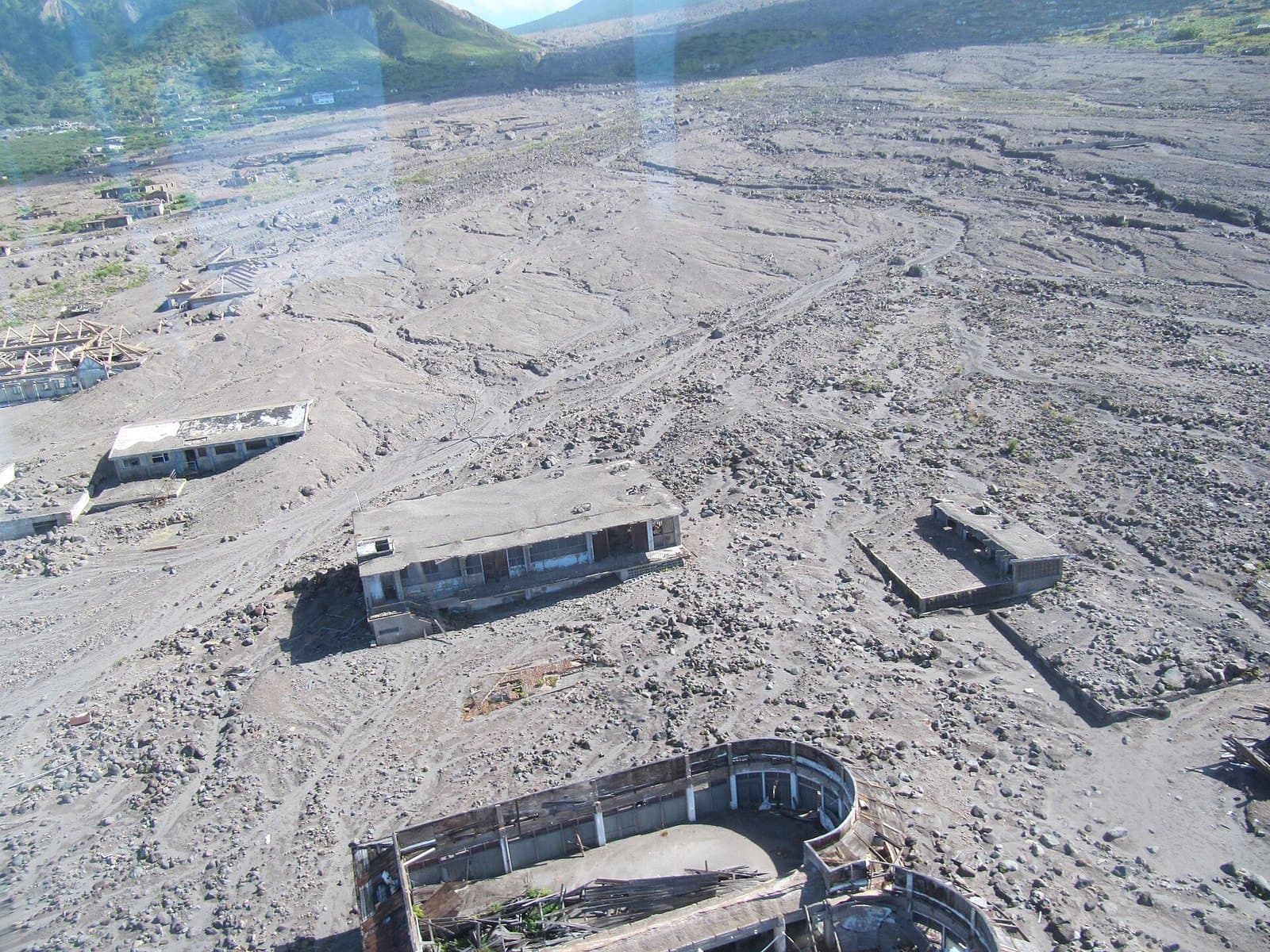 The buried town of Plymouth, Montserrat, seen from the air: roofless concrete buildings standing half-submerged in a grey plain of volcanic ash and rubble