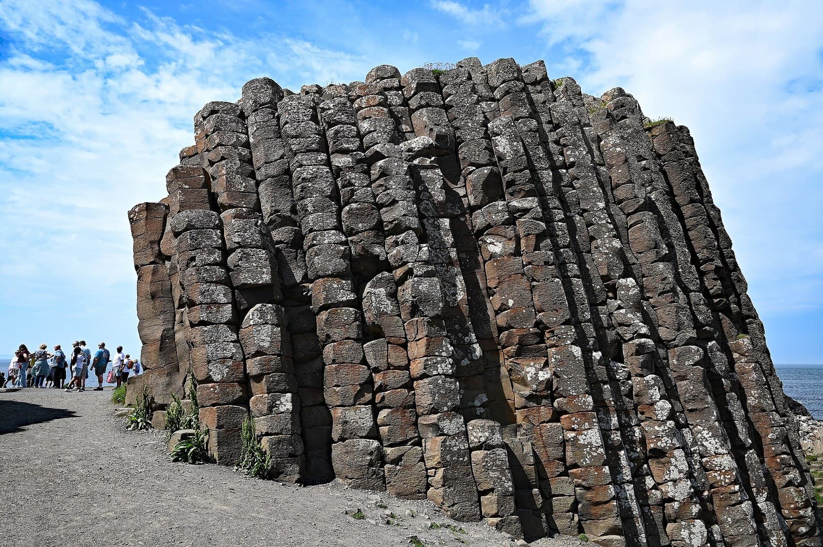 The stepped basalt columns of the Giant's Causeway on the County Antrim coast, with a small group of visitors on the path beside them and the sea beyond