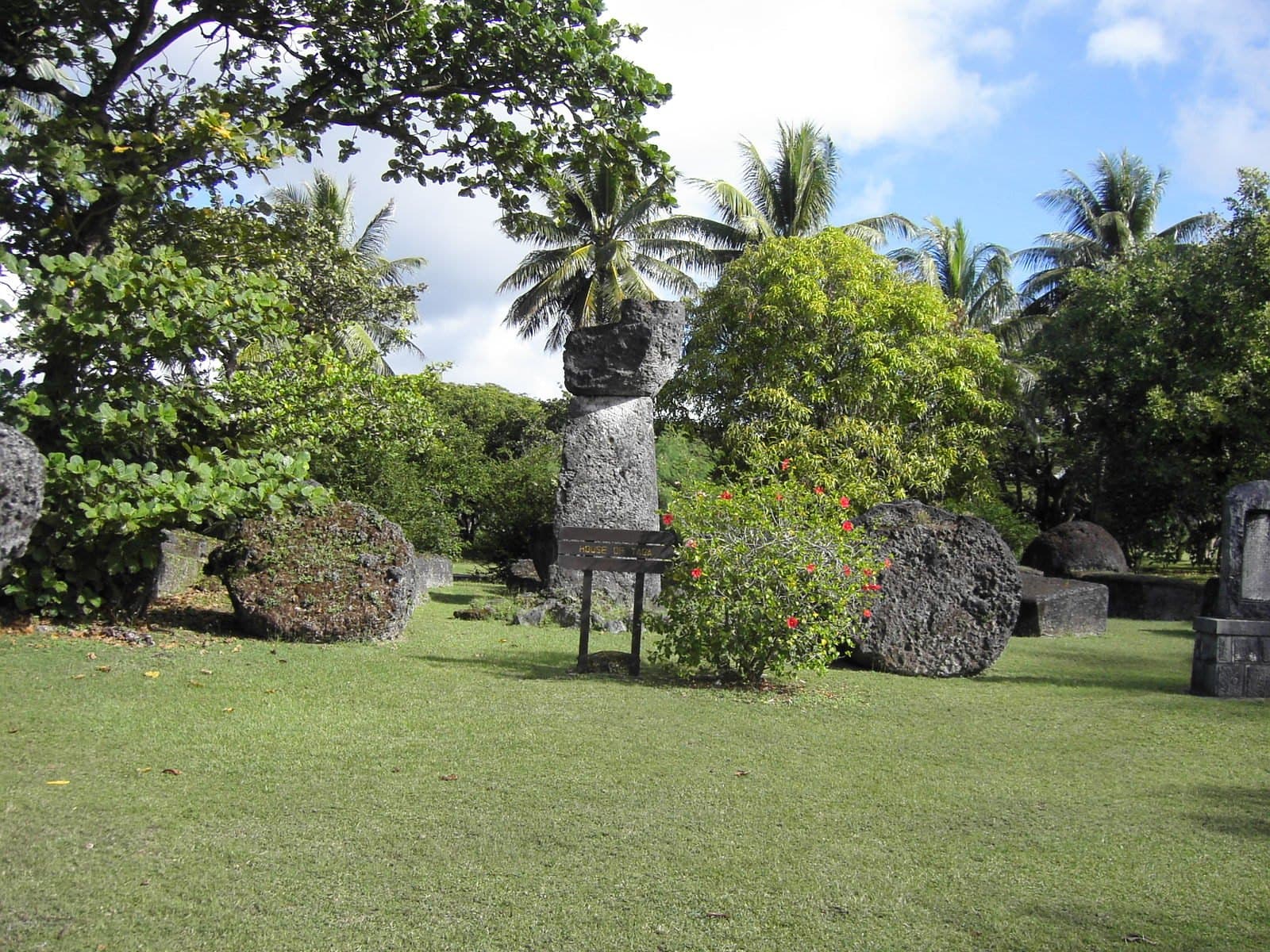 The standing latte stone at the House of Taga on Tinian, with fallen limestone pillars and capstones lying on the lawn around it
