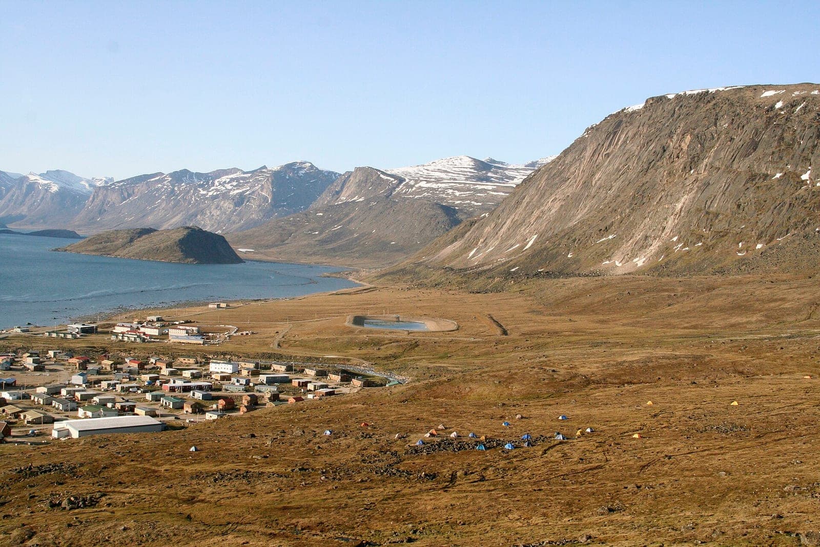 The community of Pangnirtung on Baffin Island seen from the hillside above, houses along the shore of Pangnirtung Fjord with snow-streaked mountains beyond