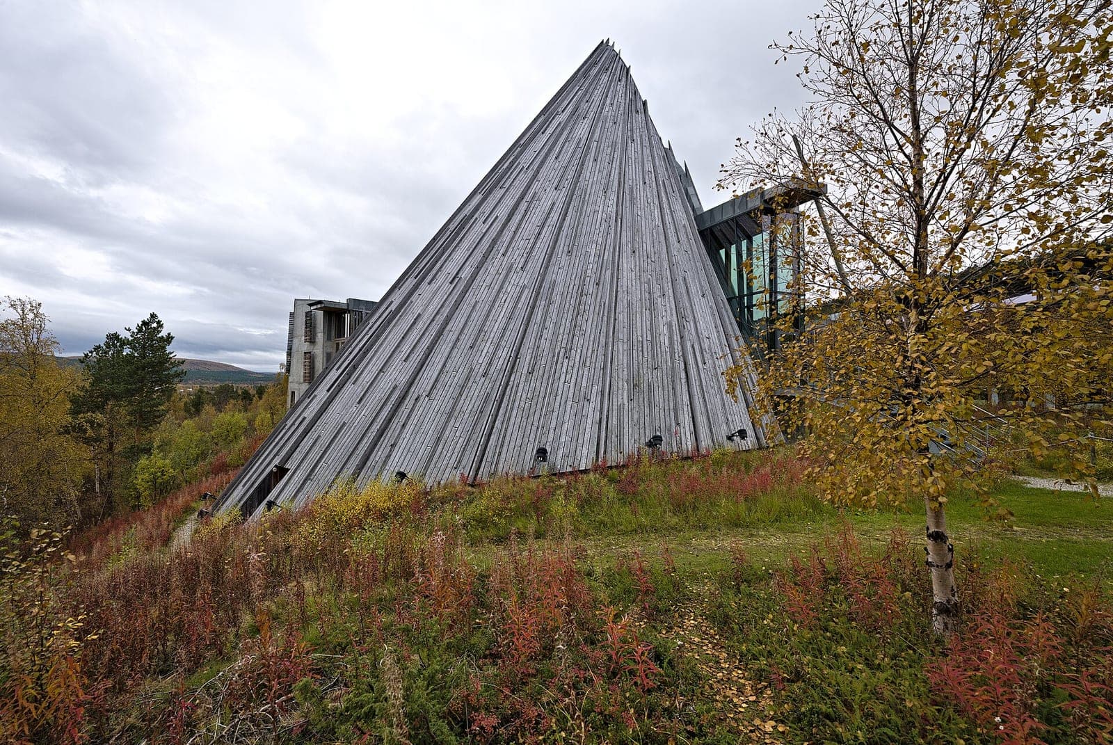 The timber cone of the plenary hall at the Sámi Parliament of Norway in Kárášjohka, shaped like a lávvu, above autumn heath and birch