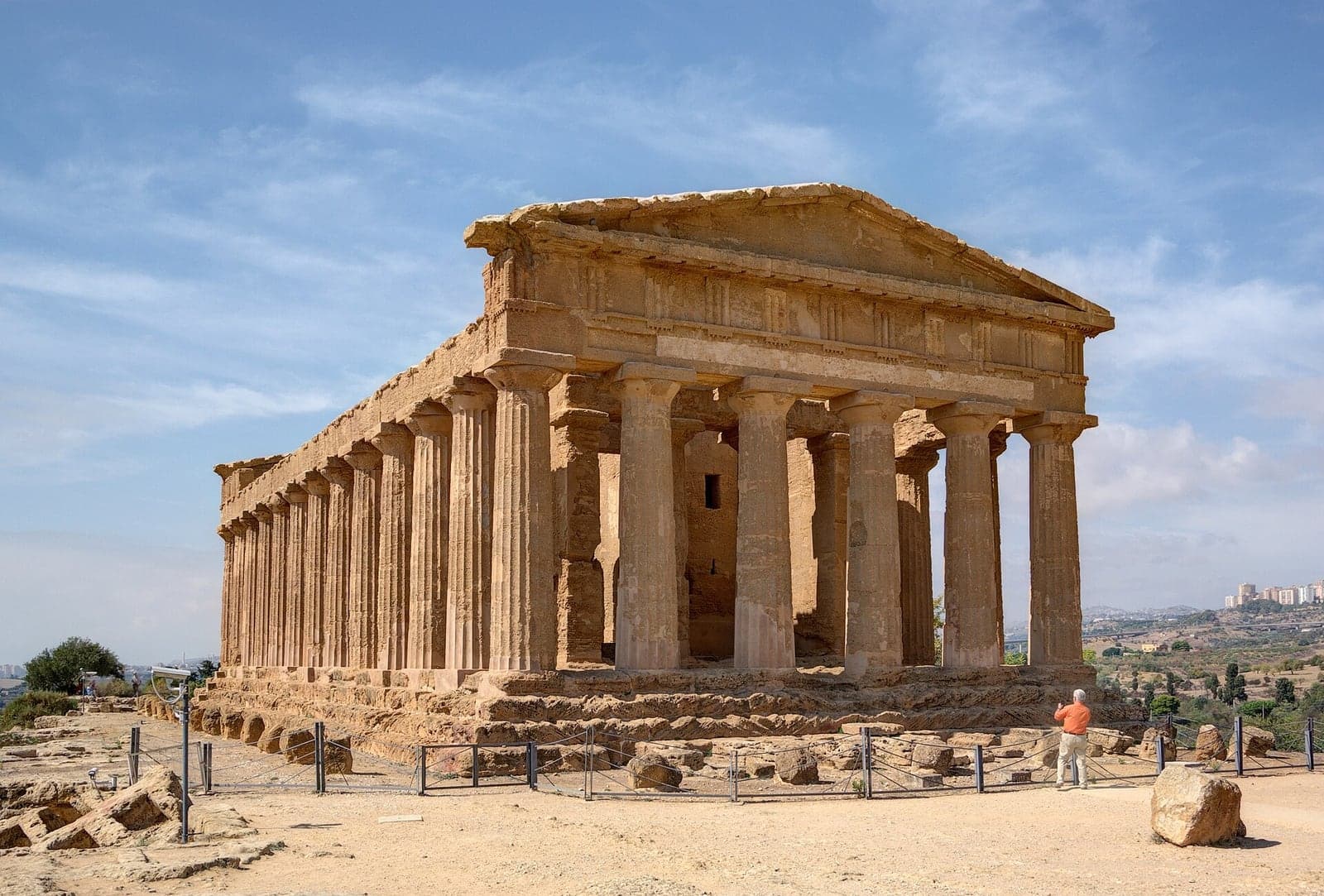 The Doric Temple of Concordia at Agrigento, its columns and both pediments standing complete on a ridge of pale rock, with a single visitor at the base for scale