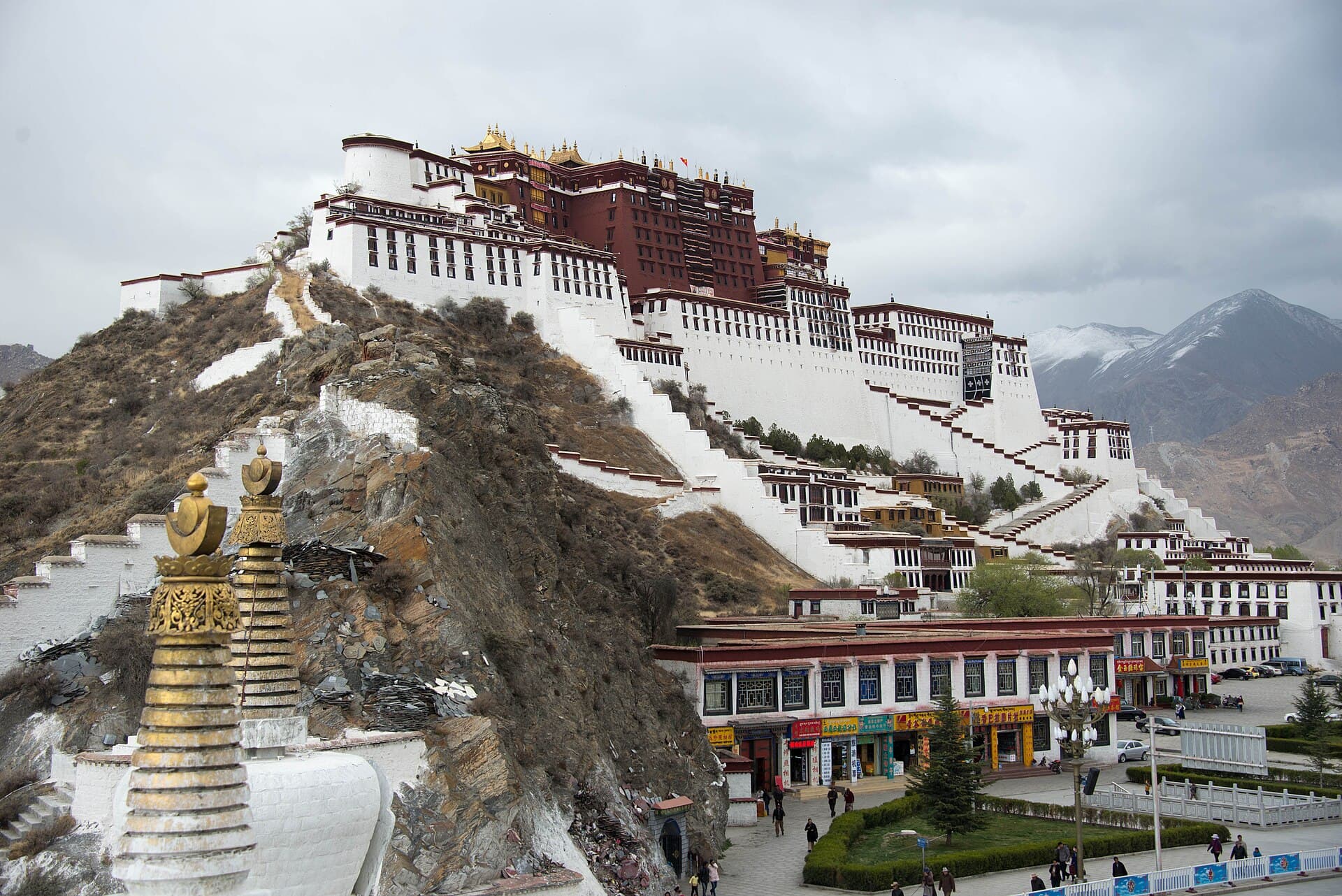 The Potala Palace in Lhasa, its white and ochre-red blocks rising in tiers up a rocky hill above whitewashed stupas and the streets below