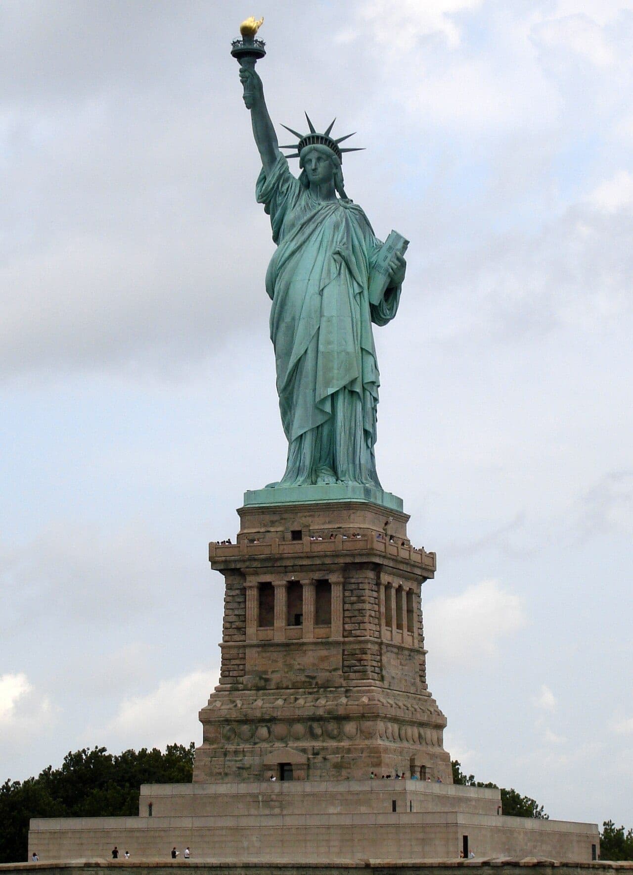 The Statue of Liberty on Liberty Island, its copper surface weathered to green, holding a torch aloft against a clear sky