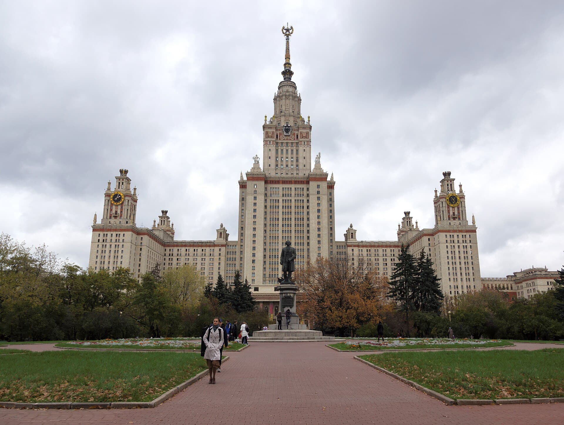 The Main Building of Moscow State University on the Sparrow Hills, its tiered stone tower and spire seen across the approach, with the statue of Mikhail Lomonosov standing in front